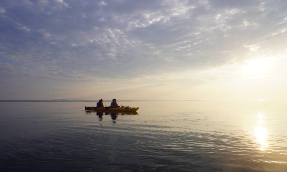 Kayak double flottant sur une mer calme au lever du soleil dans l'archipel de Mingan